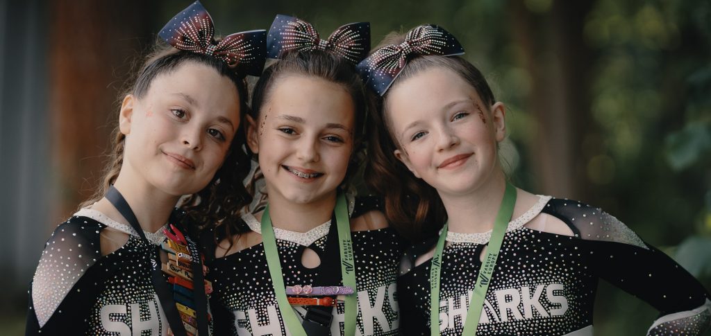 Drei junge Sharks-Cheerleaderinnen mit Medaillen nach einem Wettkampf